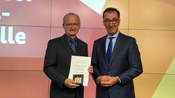 Bundesminister Özdemir steht mit Prof. Dr. Thomas Mettenleiter auf der Bühne, Prof. Dr. Thomas Mettenleiter hält die Urkunde und die Professor Niklas-Medaille in die Kamera