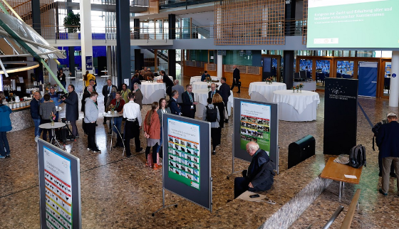 Halle im Kongres-Center: Einige Personen unterhalten sich an Stehtischen, daneben stehen Plakatwände zum Thema. Im Hintergrund sieht man auf einer Leinwand den Titel " Kongress zur Zucht und Erhaltung alter und bedrohter einheimischer Nutztierrassen".