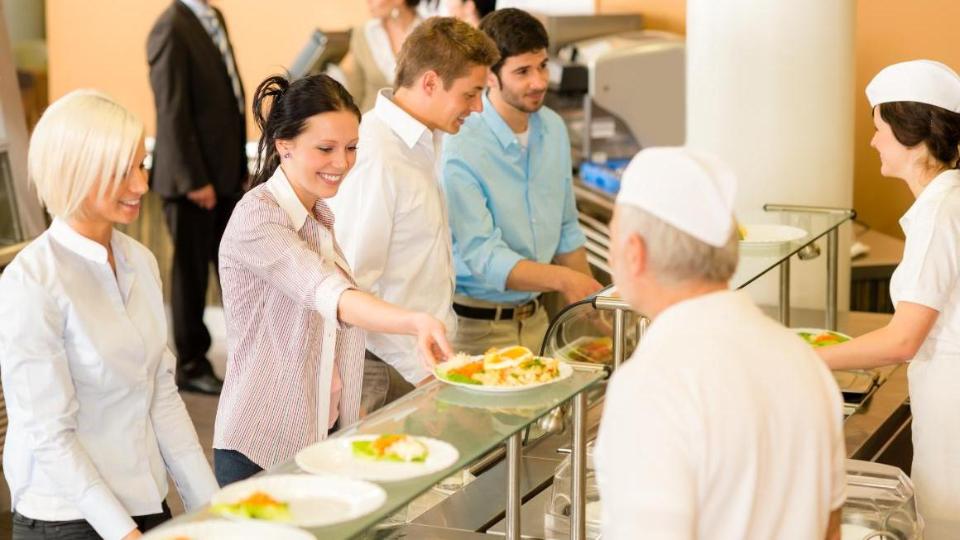 Eine Frau an der Essensausgabe einer Kantine nimmt sich einen gefüllten Teller