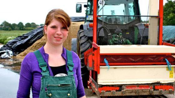 Junge Landwirtin neben Schlepper mit Siloschneider