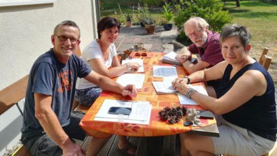 Zwei Frauen und zwei Männer sitzen im Garten auf der Terrasse an einem Tisch, auf dem Unterlagen und ein Smartphone liegen