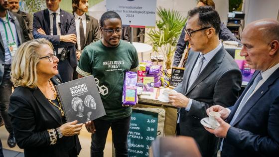 Bundesminister Özdemir hält eine Kaffeetasse in der Hand, ihm wird ein Buch präsentiert mit dem Titel "Strong woman - Behind a strong Coffee"