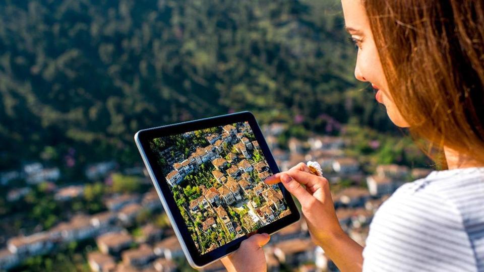 Frau hält ein Tablet und fotografiert damit ein Dorf