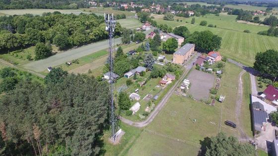 Funkmast in einer ländlichen Region mit Feldern, Bäumen und Gebäuden