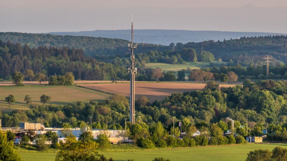 Blick über Felder in Richtung Wald im Vordergrund dein Funkmast