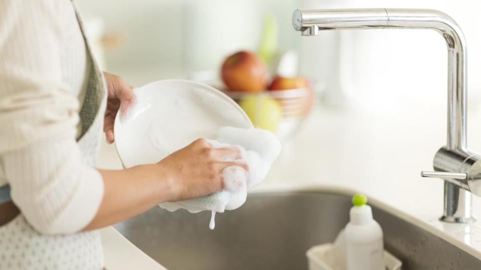 Ein Teller wird unter einem Wasserhahn mit einem Schwamm abgewaschen