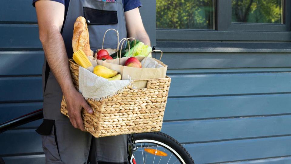 Ein Mann steht vor einem Fahrrad und hält einen Korb mit Lebensmittel.