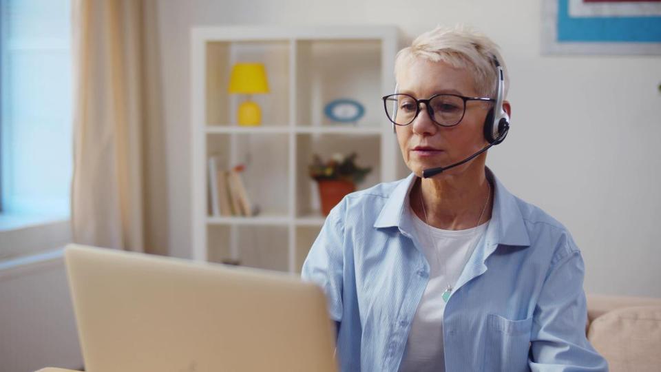 Eine Frau guckt auf einen Laptopbildschirm und hat ein Headset auf.