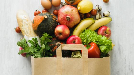 Various foods in a paper bag: fruits, vegetables, eggs, bread