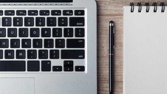 A smartphone, a keyboard, a pen and a notebook are laying on a table