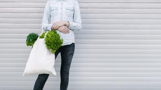 A woman is holding a fabric bag filled with vegetables in her hands