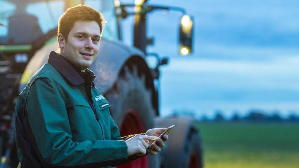 Farmer with smartphone in front of tractor