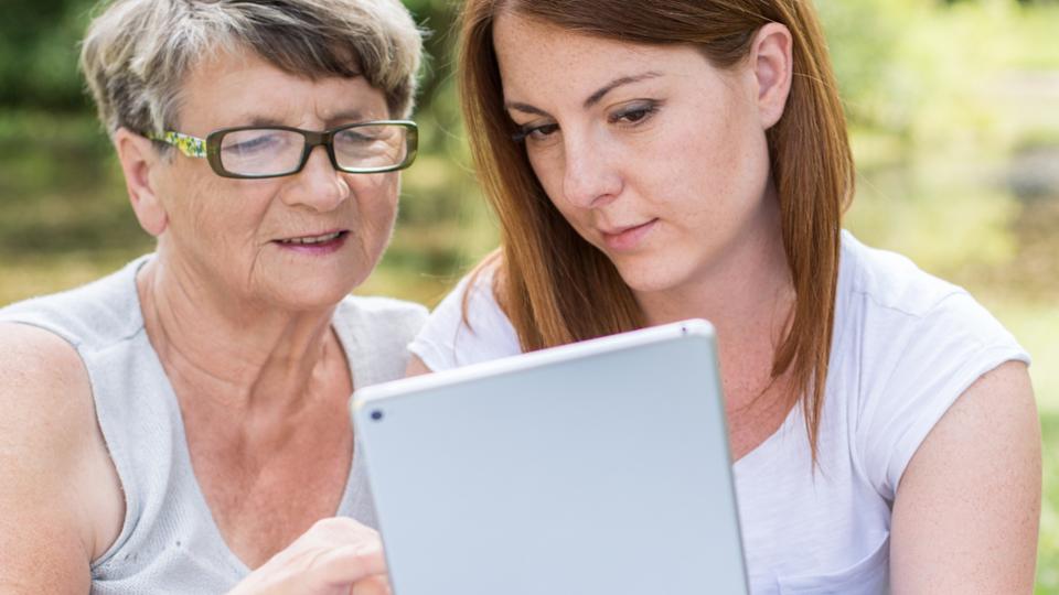 A young woman shows an older woman something on a tablet