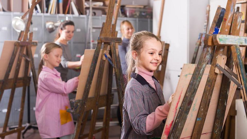 Two girls and two women are standing in front of their easels and paint